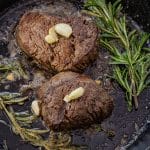 two filet mignons in a cast iron pan topped with a few garlic cloves