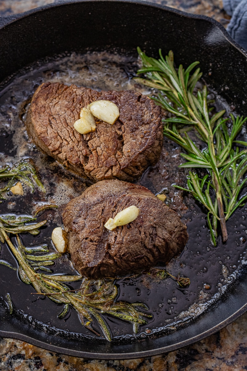 two filet mignons in a cast iron pan topped with a few garlic cloves