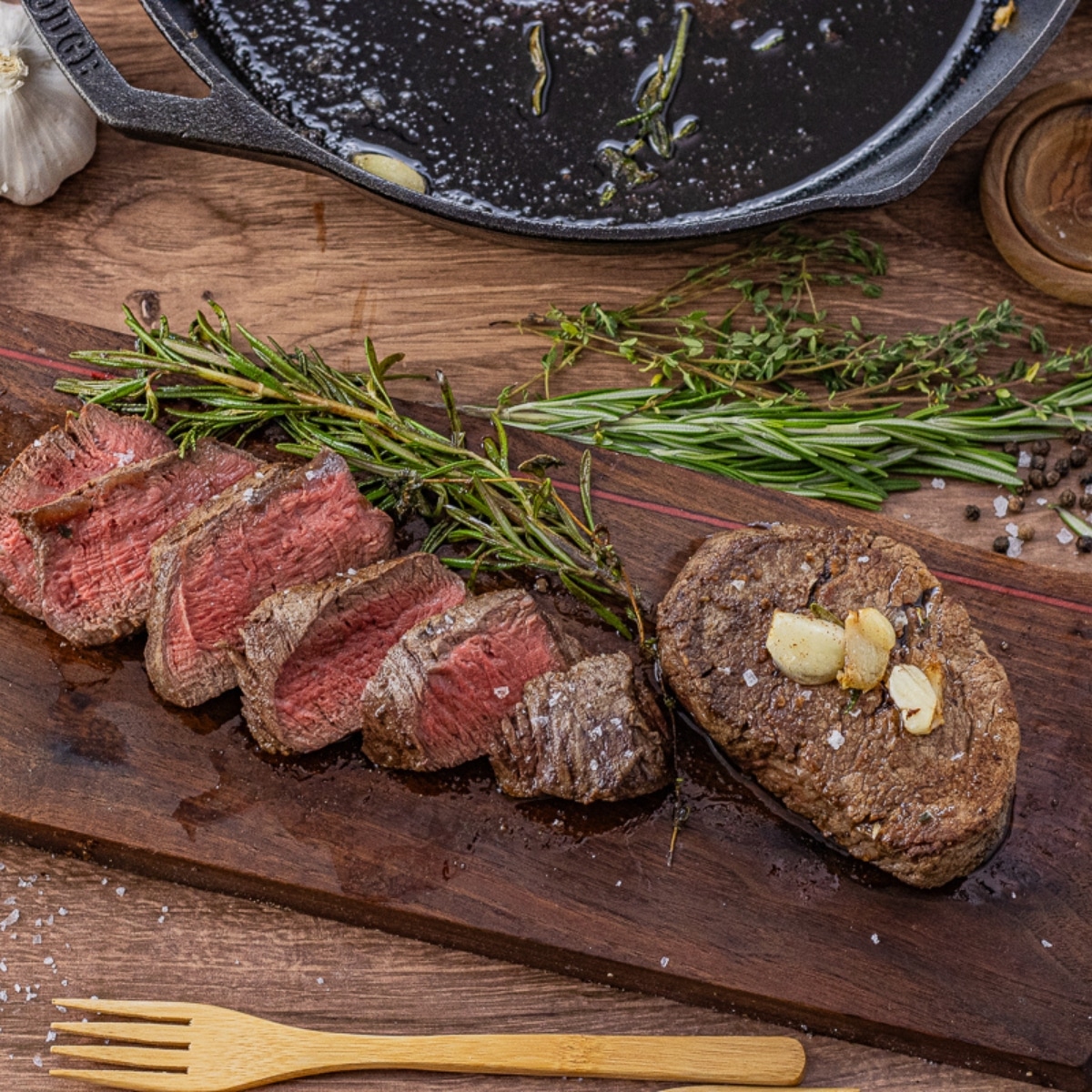 one whole and one sliced filet mignon on a wooden cutting board