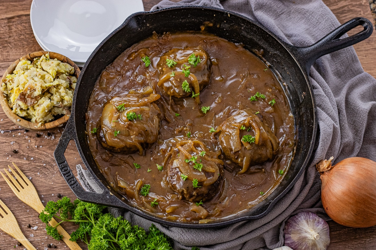 hamburger steaks in onion gravy in a cast iron skillet