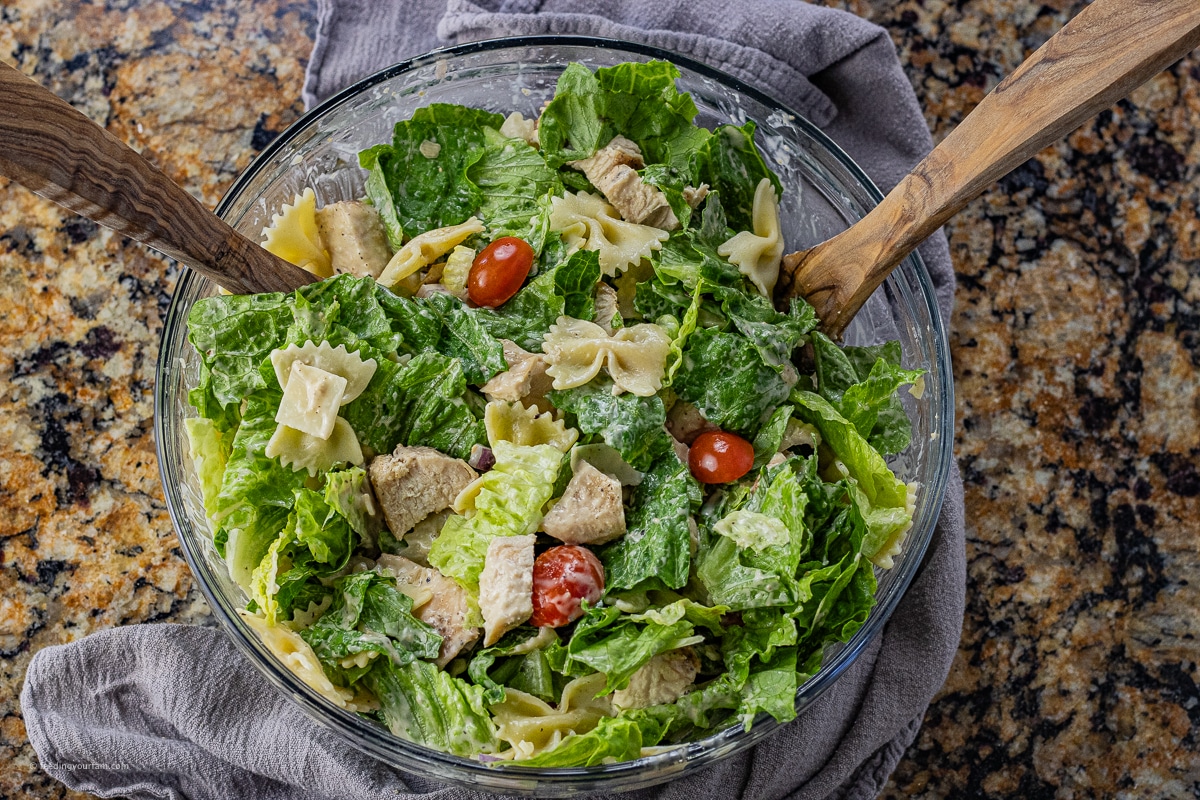 caesar salad with chicken and bowtie pasta in a large glass serving bowl