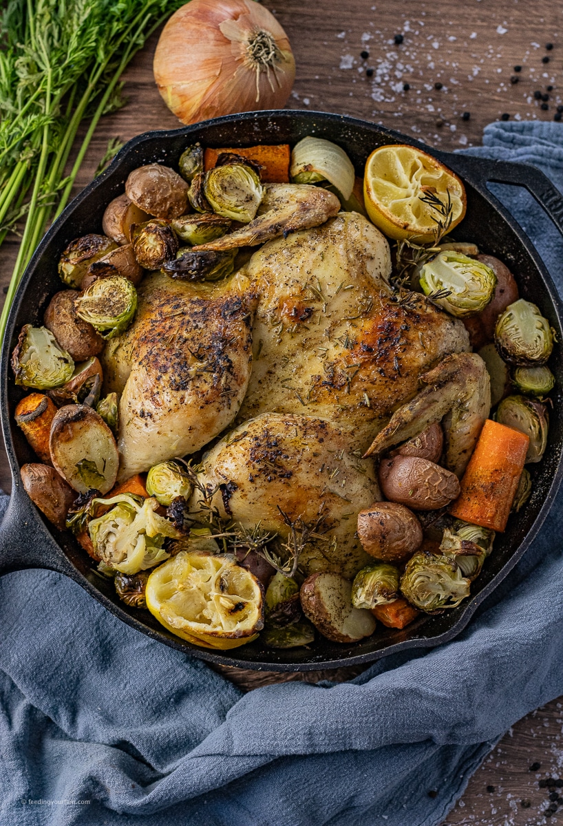 whole chicken in a cast iron skillet with potatoes, carrots and brussels sprouts baked around it