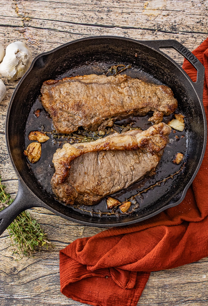 two new york steaks cooked in a cast iron skillet with garlic and thyme sprigs