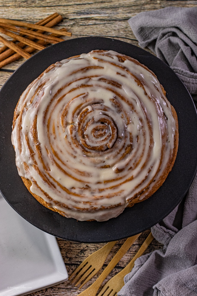 giant cinnamon roll cake frosted and sitting on a black plate