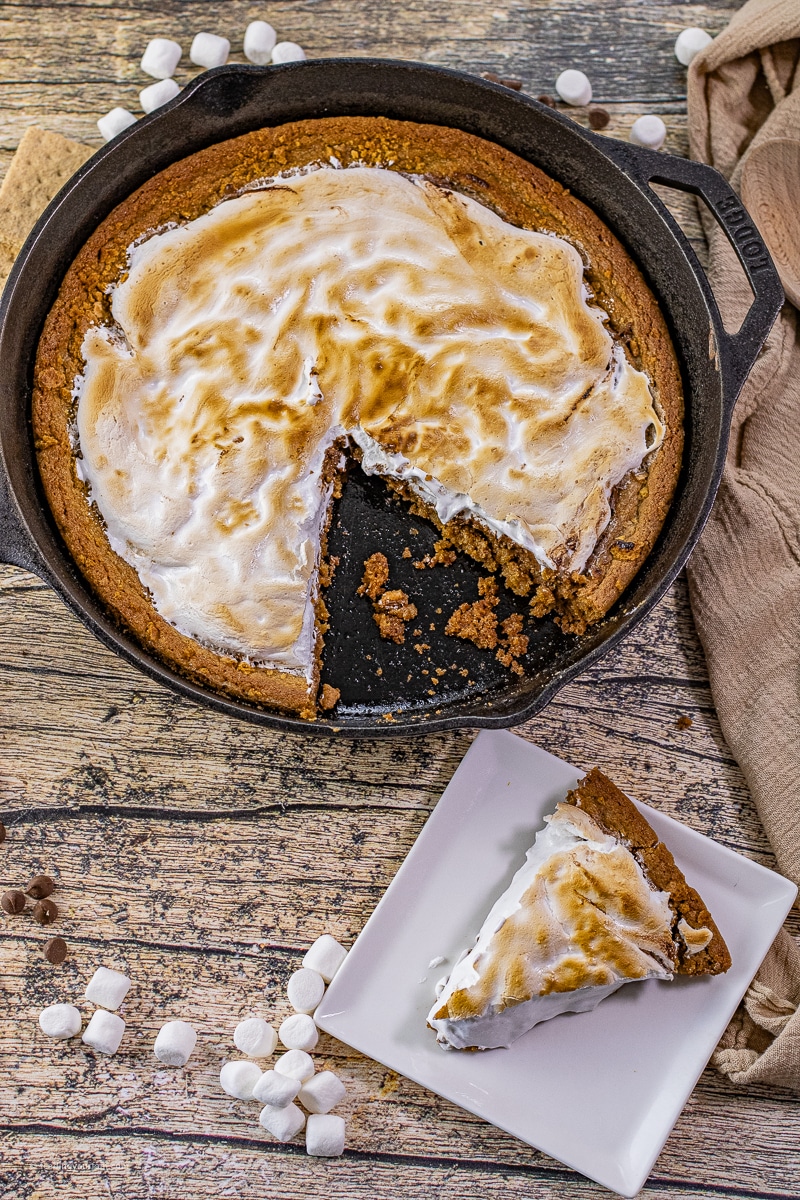 Warm slice of skillet s’mores cookie showing gooey layers of graham cookie, chocolate, and marshmallow