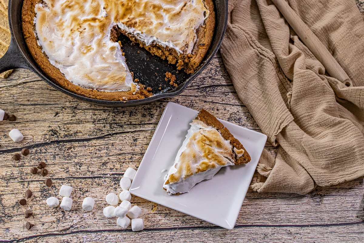 Warm slice of skillet s’mores cookie showing gooey layers of graham cookie, chocolate, and marshmallow