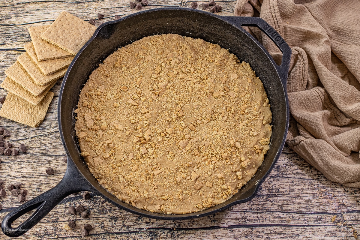 Unbaked graham cracker cookie dough pressed evenly into a black cast iron skillet