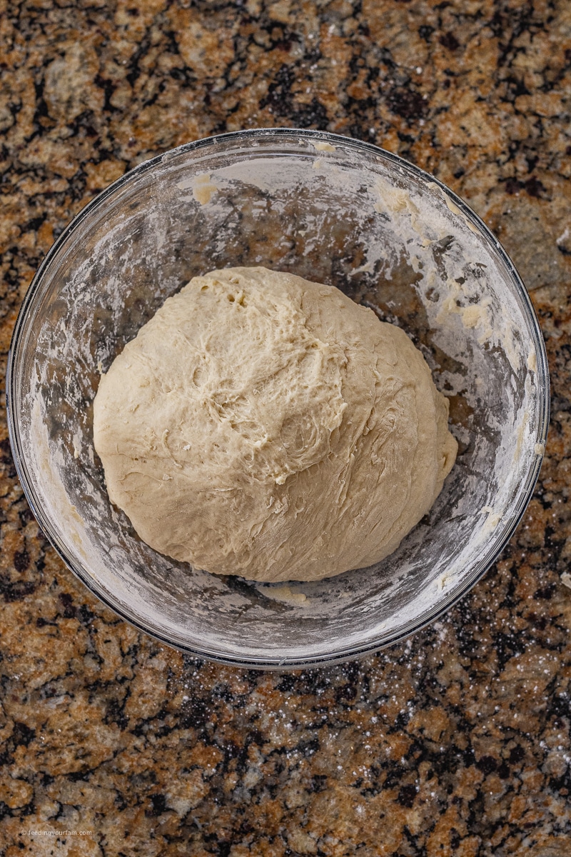 round ball of homemade bread dough in a glass mixing bowl