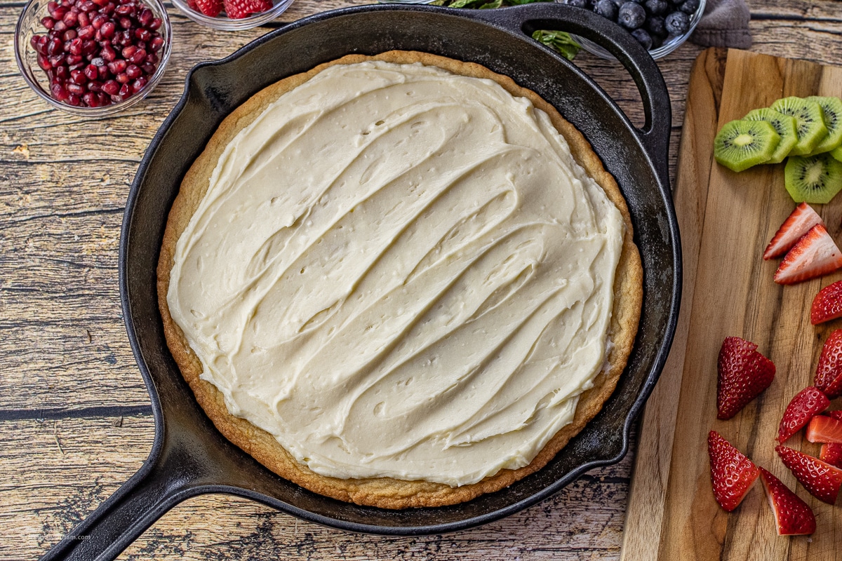 fruit pizza topped with cream cheese frosting in a cast iron skillet