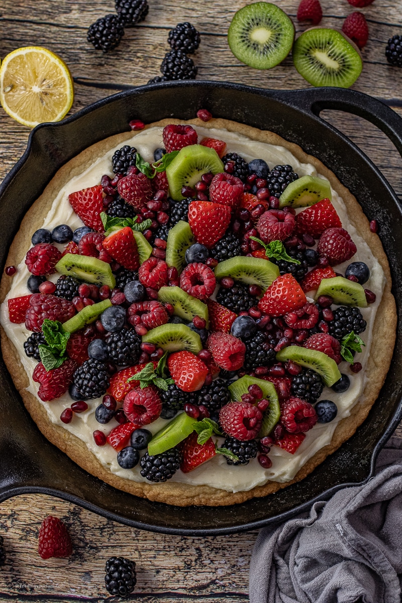 fruit pizza baked in a cast iron skillet topped with fresh berries and kiwi fruit