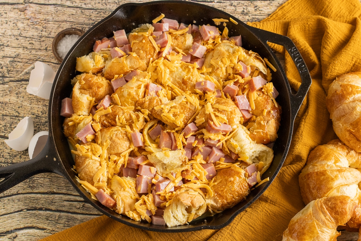 uncooked ham and cheese croissant casserole in a cast iron skillet