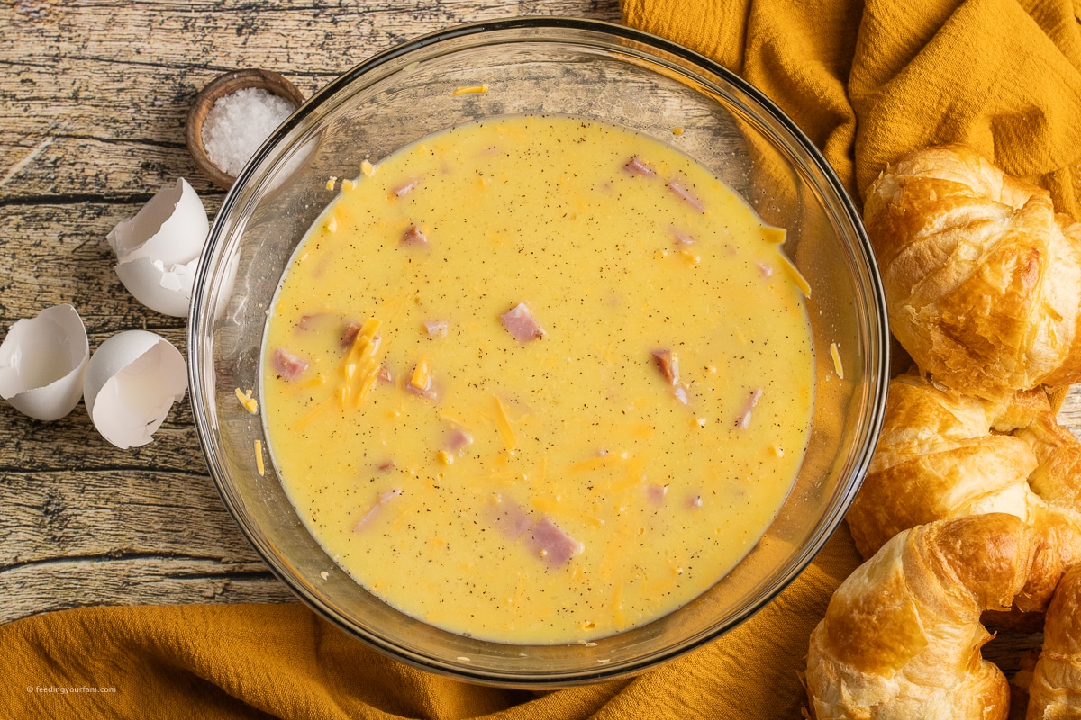 eggs, milk, cheese and ham in a mixing bowl