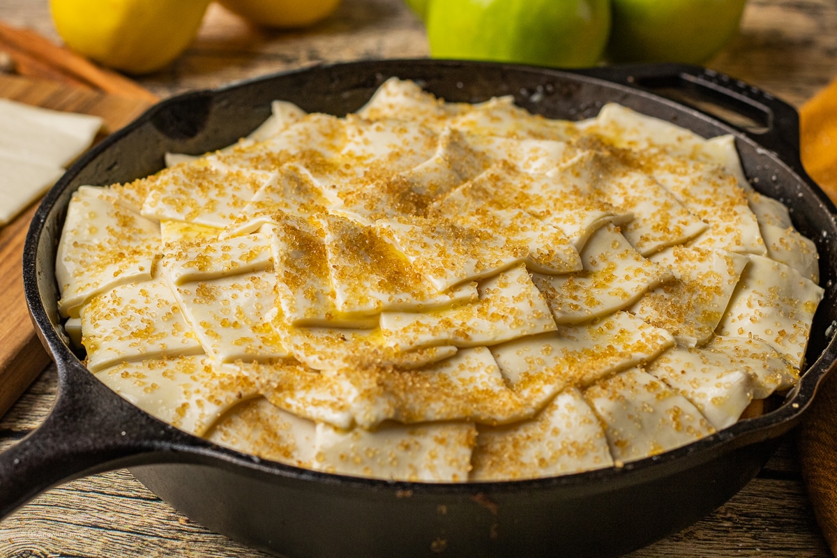 unbaked skillet apple pie topped with sliced pieces of puff pastry in a cast iron skillet