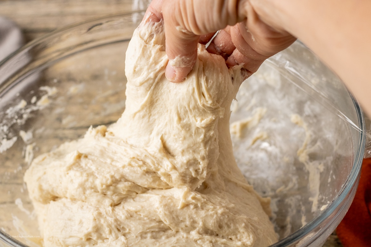 stretching and folding dough in a glass mixing bowl