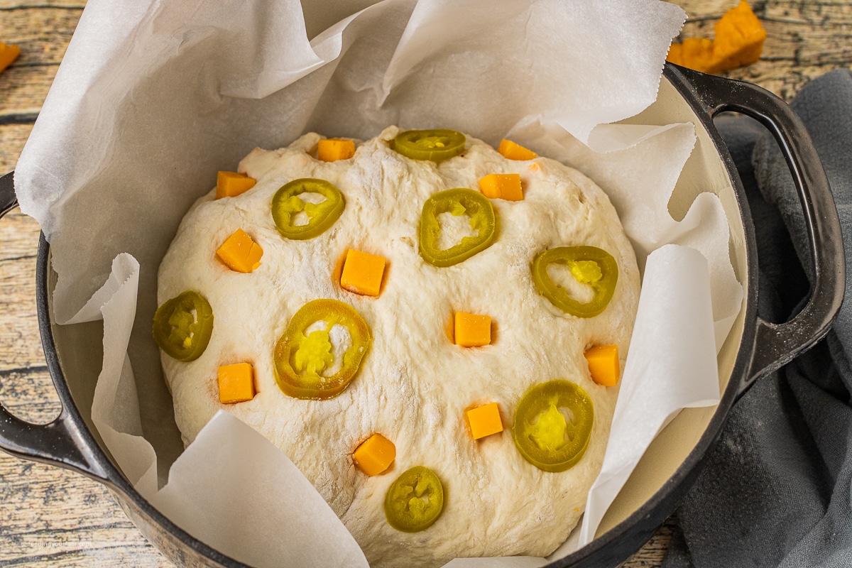 Dutch oven jalapeño cheddar bread loaf uncooked with pieces of sharp cheddar cheese and sliced jalapenos