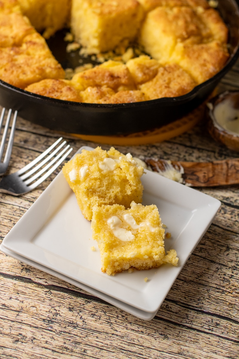 cornbread butter swim biscuits baked in a cast iron skillet, one split in half with butter on top